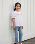 7-year-old Asian girl standing against white wooden wall