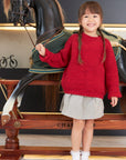 Child in a red sweater standing next to a decorative horse statue indoors.