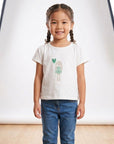 Young girl wearing a white t-shirt with a graphic design and blue jeans on a plain background