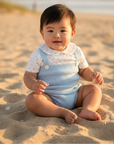 Asian baby boy in light blue knitted romper with polka dot shirt seated on sand