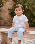 Asian baby boy in light blue pants and white duck top on wooden bench over Spanish tiles