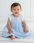 Asian baby girl in blue gingham dress seated outdoors with white wooden background
