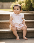 Asian baby girl in pale pink romper with white lace details seated on stairs