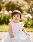 Asian baby girl in pink and white eyelet dress seated outdoors