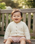 Asian baby girl wearing cream cardigan with pink shorts on outdoor bench