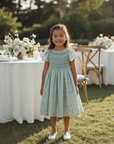 Asian girl facing front in sage green smocked dress at celebration