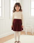 Asian little girl in burgundy velvet skirt with white wood background