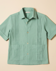 Flat lay product photo of sage green guayabera shirt on beige background