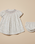 Flat lay product photo of smocked dress and bloomers set on beige background
