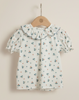 Floral blouse with ruffled collar on a wooden hanger against a beige background