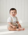 Lifestyle photo of Asian baby boy wearing beige suspender shorts with white Mao collar shirt