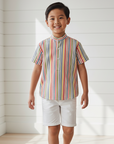 Lifestyle photo of Asian boy wearing colorful striped Mao collar shirt with unbuttoned collar and white shorts
