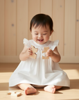 Realistic luxury lifestyle photo of Asian baby girl with toy, seated on floor with wooden beige background