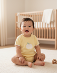 Smiling Asian baby girl in yellow romper with toy on floor