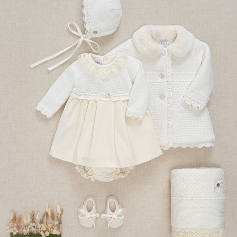 Baby outfit set with coat, dress, bonnet, and shoes on a beige background