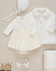 Baby outfit set with coat, dress, bonnet, and shoes on a beige background
