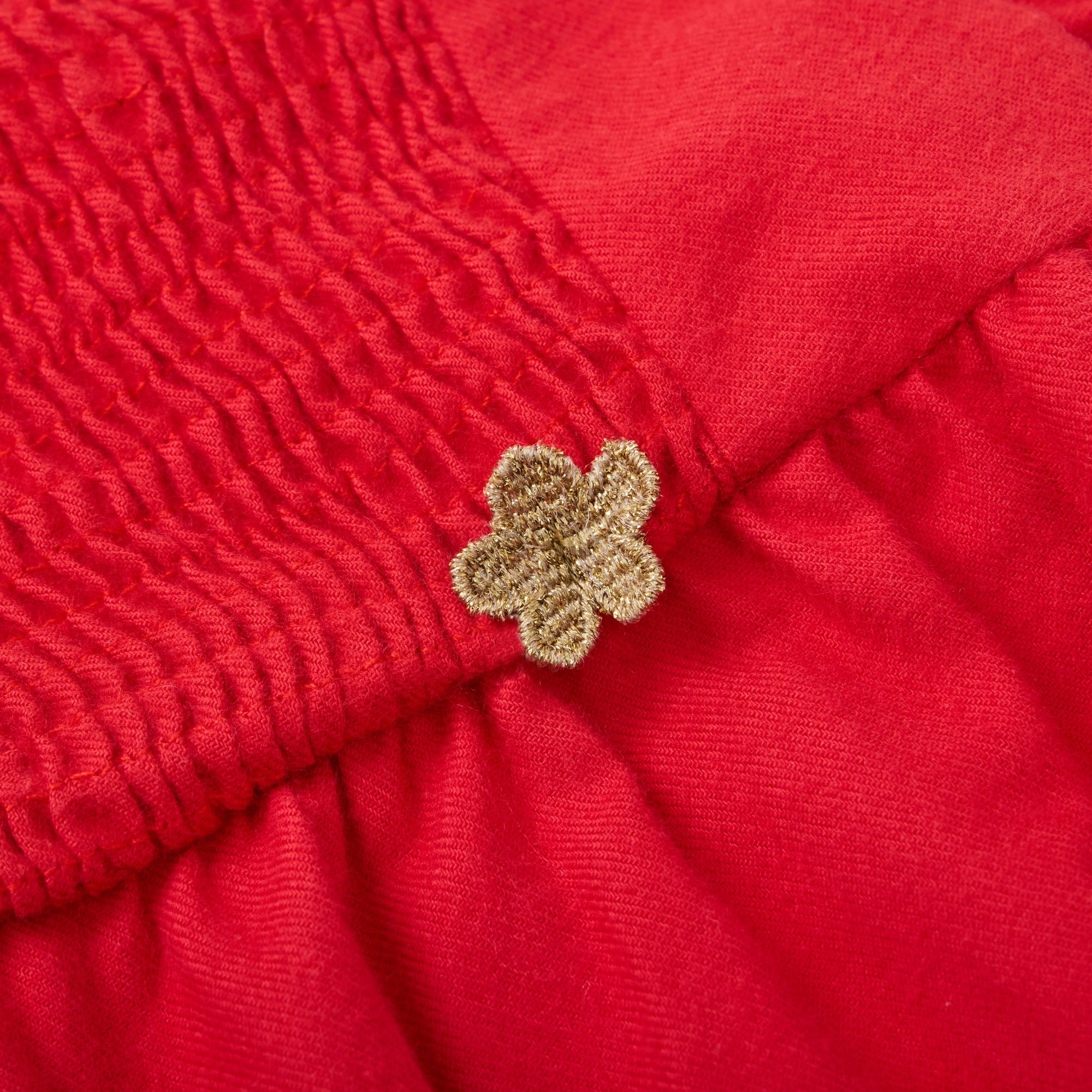 Close-up of a red fabric with a textured pattern and a gold flower-shaped button.