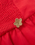 Close-up of a red fabric with a textured pattern and a gold flower-shaped button.