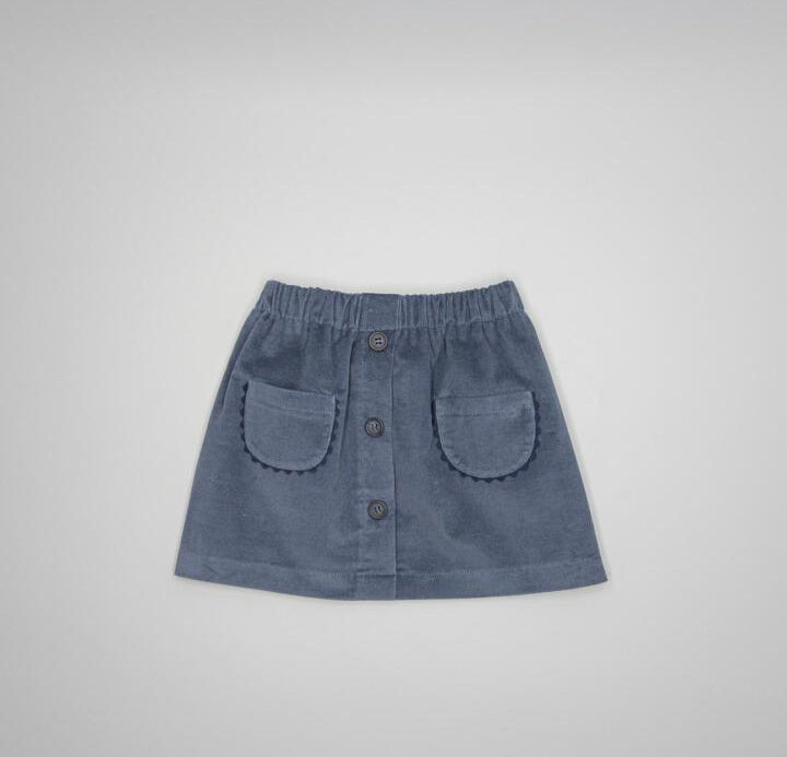 A slate blue corduroy mini skirt with an elastic waistband, button-front closure, and two decorative patch pockets, shown flat on a light gray background.