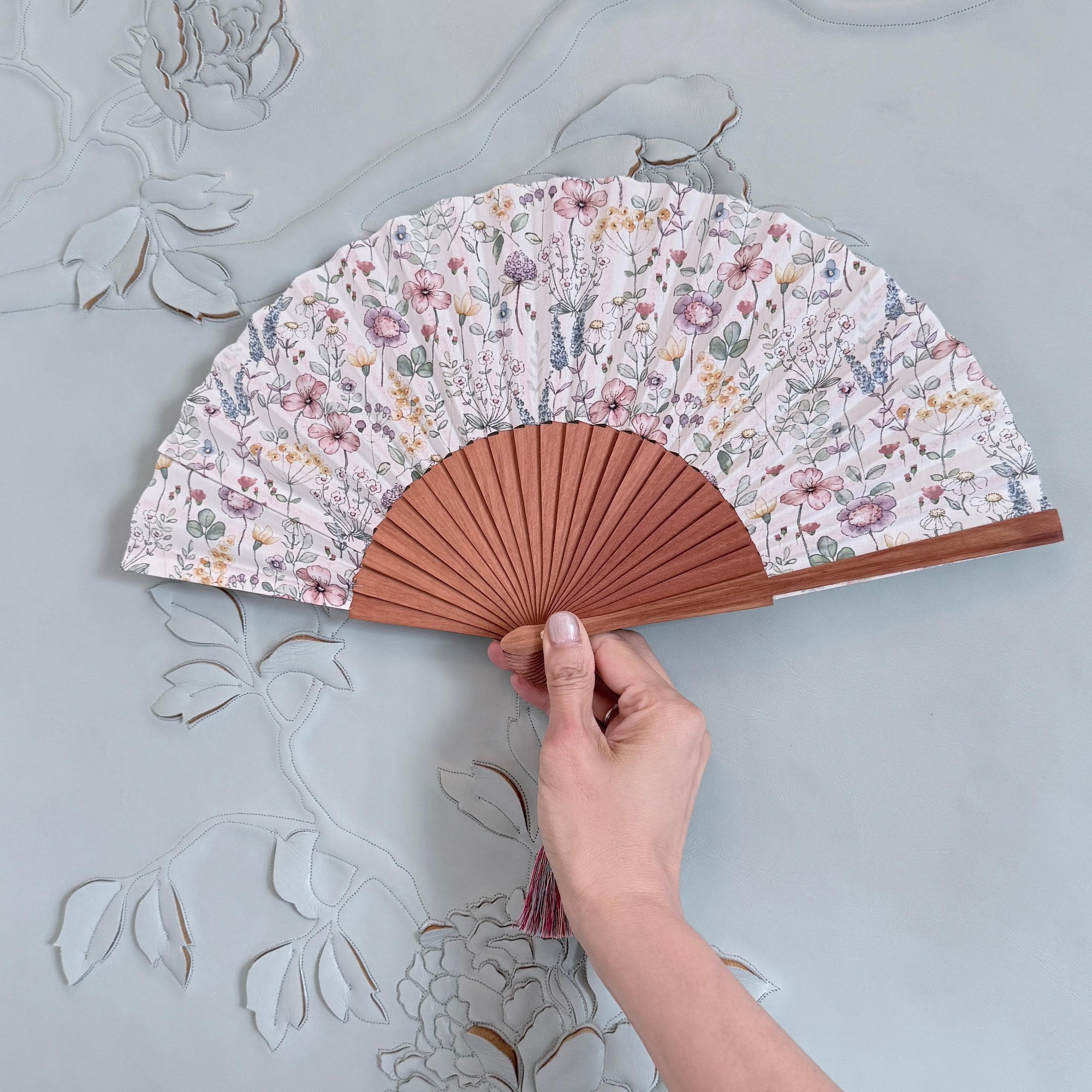 Hand holding a floral-patterned fan against a decorative wall.