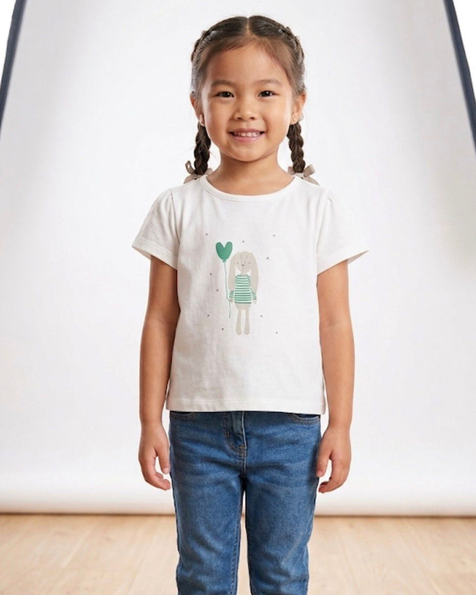 Young girl wearing a white t-shirt with a graphic design and blue jeans on a plain background