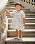 Asian baby girl in cream floral dress on circular staircase
