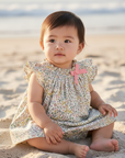 Asian baby girl in Liberty floral dress with bloomers seated on sand