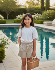 Asian girl in beige shorts with bow and white blouse in backyard with pool
