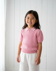 Asian girl wearing pink knit polo with white pants on white wooden background