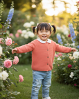 Asian toddler girl in coral cardigan outdoors in garden