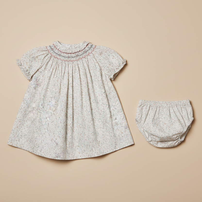 Flat lay product photo of smocked dress and bloomers set on beige background