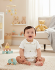 Lifestyle photo of Asian baby wearing white romper with toy on floor