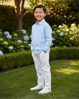 Lifestyle photo of Asian boy wearing blue shirt and white pants in elegant backyard