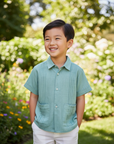 Lifestyle photo of Asian boy wearing sage green guayabera shirt with unbuttoned collar and white shorts