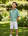 Lifestyle photo of Asian boy wearing sage green guayabera shirt with white shorts outdoors