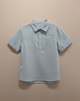 Light blue polo shirt flat lay beige background