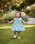 Realistic lifestyle photo of Asian baby girl wearing turquoise Liberty print dress walking on grass